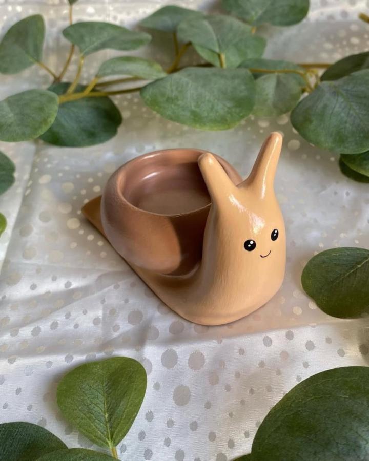 Beige and brown glazed clay snail candle holder with a smiling face by @studioyazzy. Cute and playful handmade candle accessory.