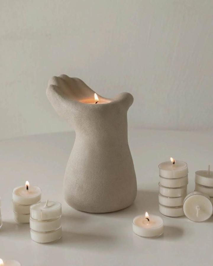 Natural beige hand-shaped candle holder on white surface with lit tealight candles from @orientaldesigngifts. Earthy and artistic clay craft.