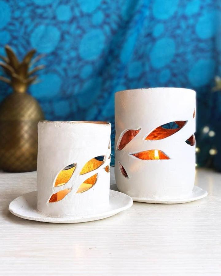 White clay candle holders with leaf cutouts and glowing candlelight from @craftygirllifehacks. Elegant handmade decor with natural light patterns.