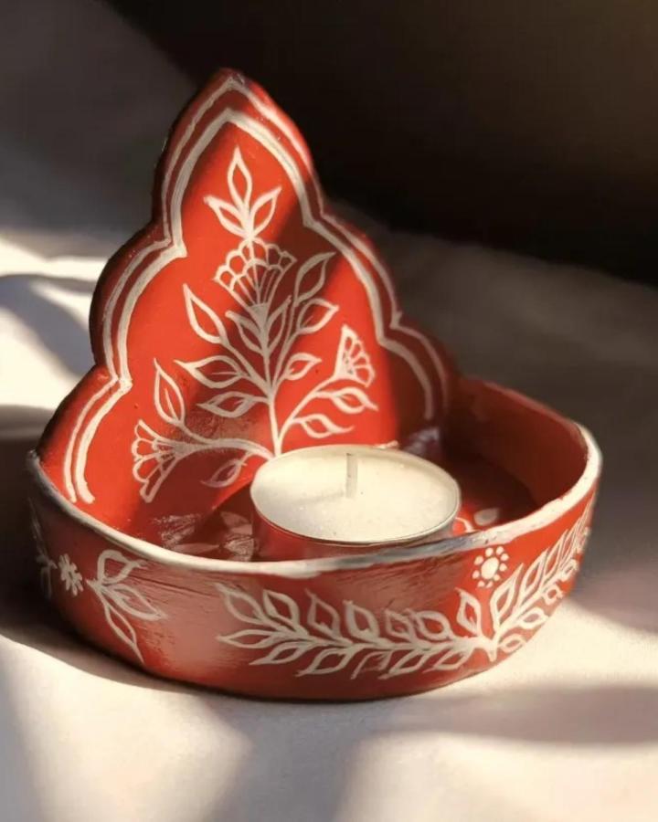 Red terracotta clay candle holder craft ideas from @adwin.studio featuring hand-painted white floral patterns and a pointed back design.