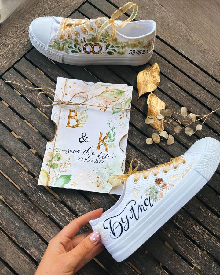 White canvas sneakers and a hand-painted botanical save-the-date card by @its.artistina featuring gold accents and personalized lettering. Fresh and creative wedding stationery alternative.