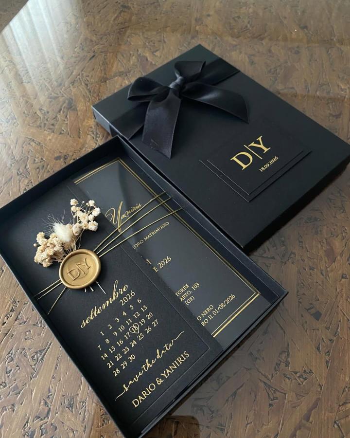 Black cardstock wedding invite with gold text, dried flowers, and wax seal from @davetiyehiraa in elegant black gift box.