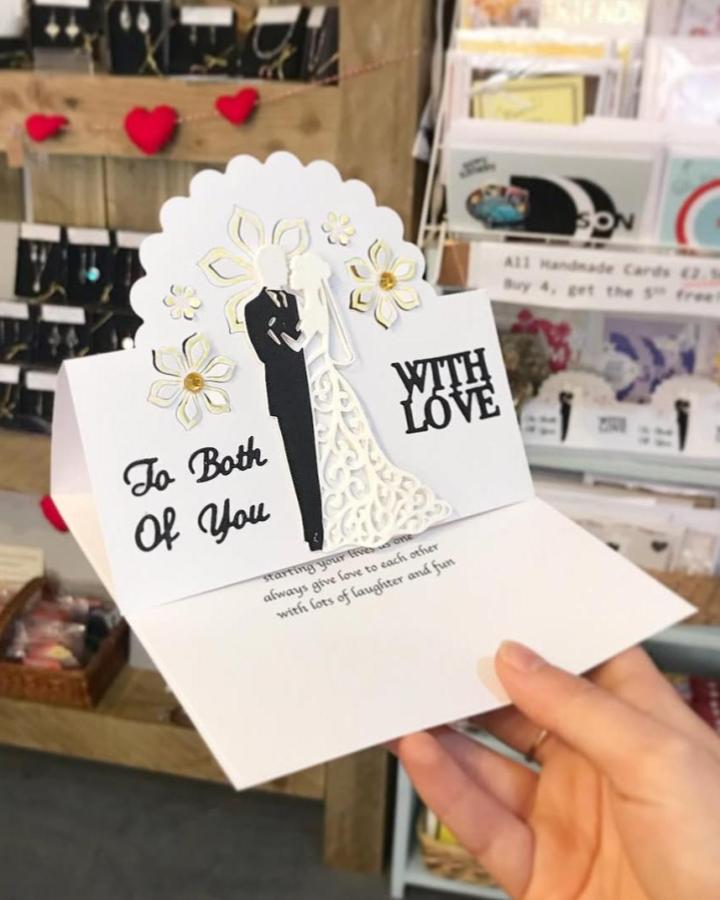 White intricate pop-up wedding card featuring bride and groom silhouette and golden floral accents by @handmadedesign.ashbourne. Elegant handcrafted paper design.