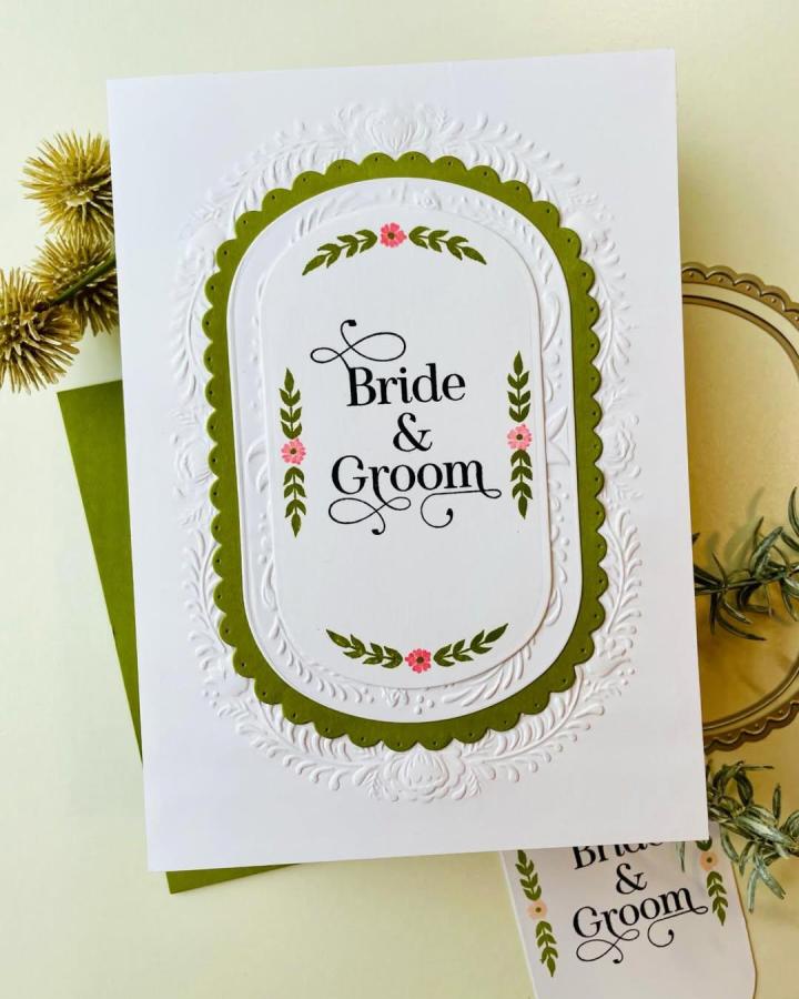 White embossed wedding card with olive green scalloped frame and pink floral details from @sandboxcards showing delicate handmade paper craft design.