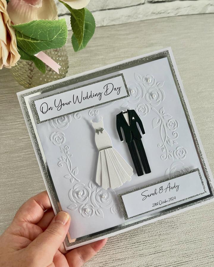 White embossed floral wedding card with silver glitter borders and 3D bride and groom paper cutouts from @emmaycardsandcrafts. Simple and elegant handcrafted invitation design.