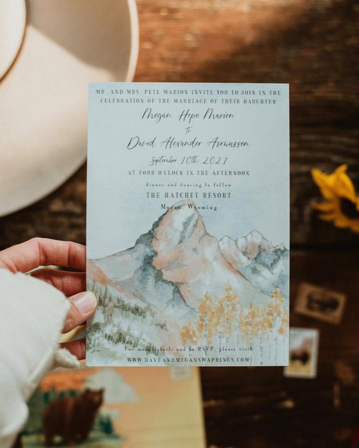 Watercolor mountain scene wedding card with rustic tones from @littlescoutcreative featuring soft grays and muted oranges diy wedding card ideas.