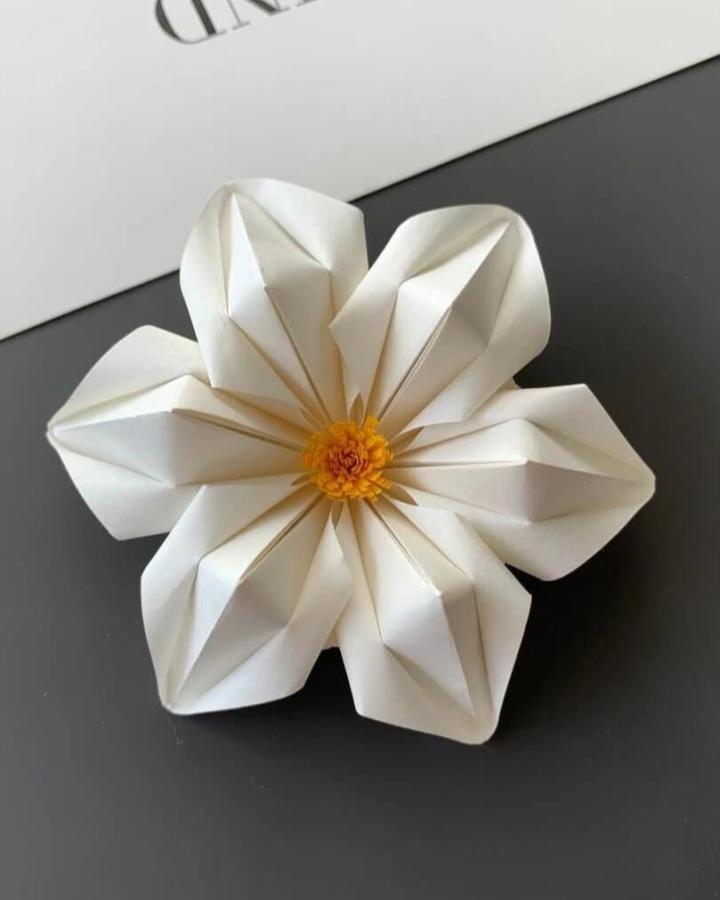 White and yellow origami flower with sharp geometric folds from @paper.art.creation. Handmade paper design with a bright floral center.