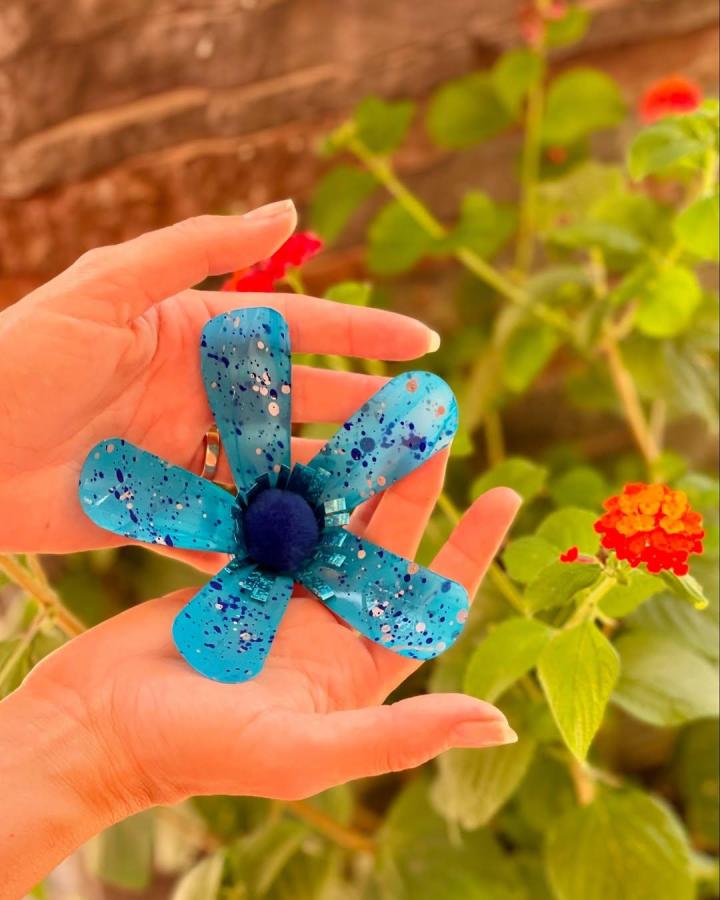 Bright blue painted recycled plastic flower craft held in hands by @kikka_arte. Handmade eco-friendly floral decoration with splattered paint design.