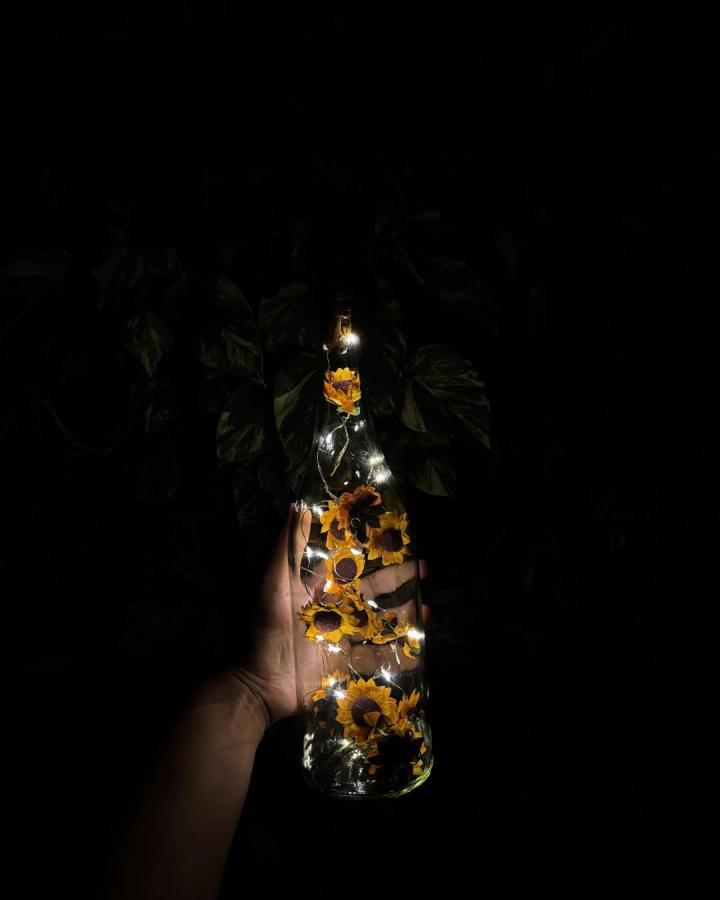 Yellow sunflower decals in a clear glass bottle with fairy lights from @artwork.jaishree. Cozy handmade light decor piece.