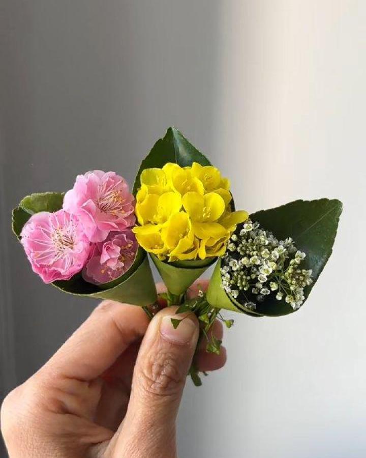 Pink yellow and white tiny flower bouquets wrapped in green leaves held by hand for delicate craft decor from @papermagicrts. Small natural floral arrangement.