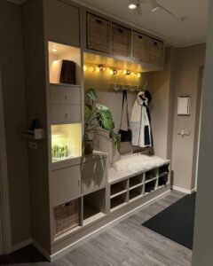 Light beige minimalist storage bench from @minimalhomelabb. Includes baskets, hooks, and glowing string lights creating a welcoming entrance space.