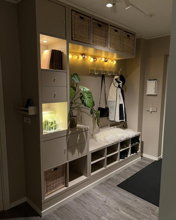 Light beige minimalist storage bench from @minimalhomelabb. Includes baskets, hooks, and glowing string lights creating a welcoming entrance space.