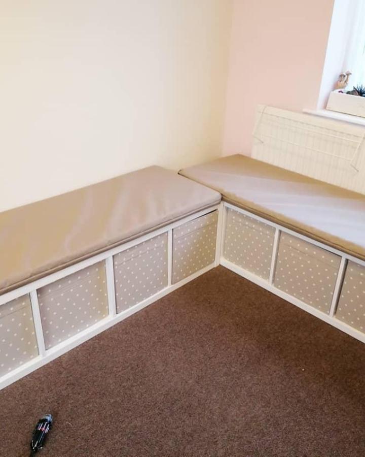 Beige cushioned corner bench with polka dot fabric panels in storage cubes from @councilhouse2home. Cozy seating with hidden storage solution.