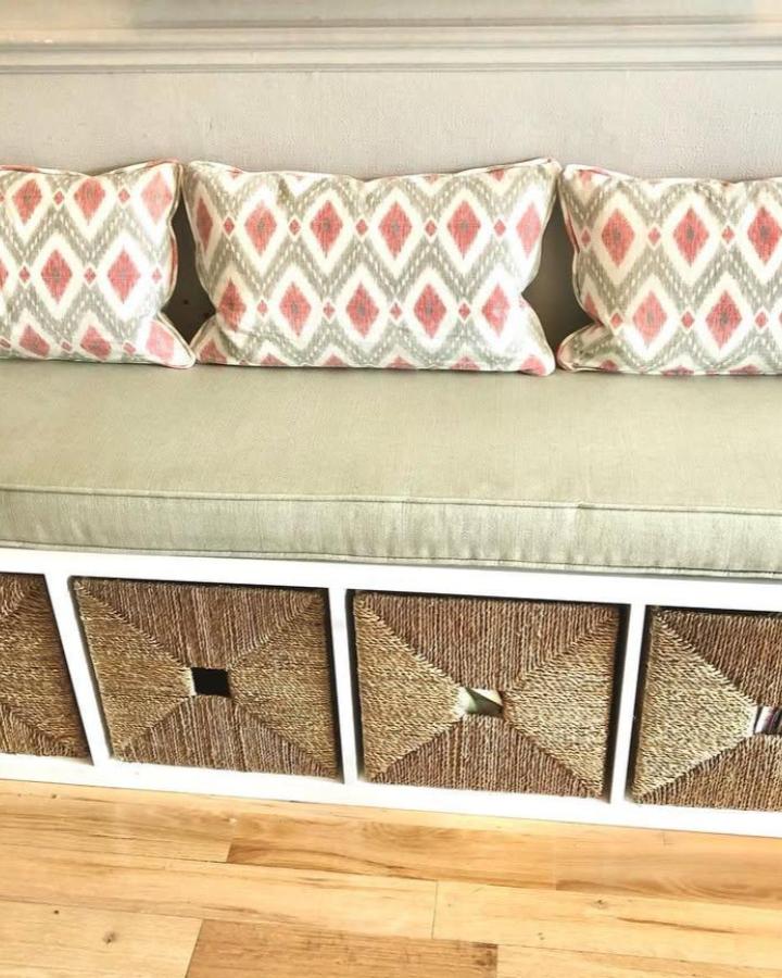 Sage cushioned bench with coral diamond patterned pillows and woven natural fiber baskets by @roombyroomdublin showing cozy storage seating.