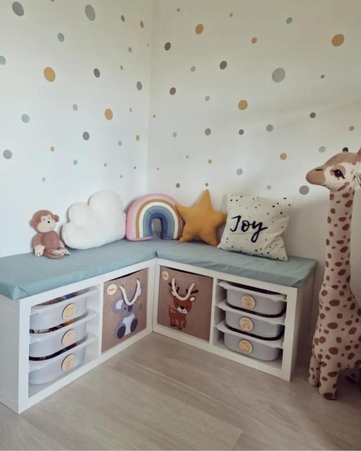 Soft pastel cushioned corner bench with animal print storage bins and playful pillows from @likkl for kids room seating and organization.