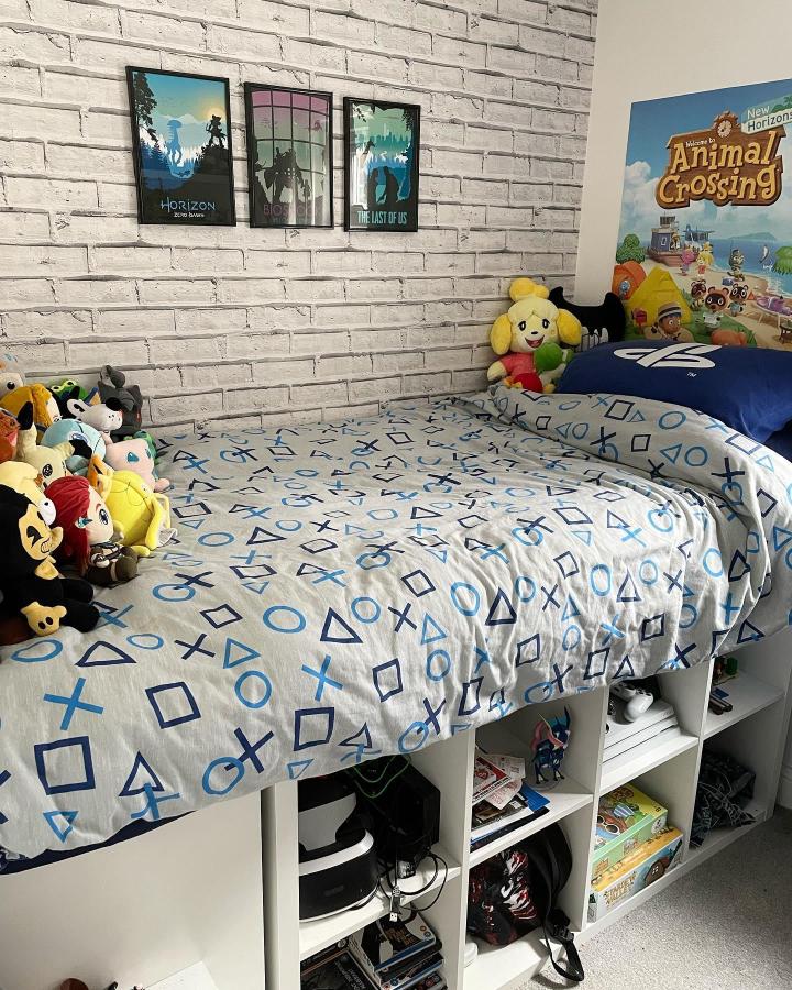 White modular storage bed with gaming-themed bedding and plush toys from @amymarieathome. Space-saving and playful bedroom solution.