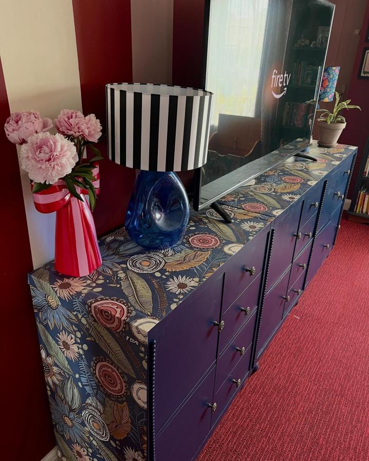 Dark navy floral covered storage unit with painted doors and decorative knobs from @athomewiththechants. Detailed TV stand with unique patterned surfaces and solid color contrast.