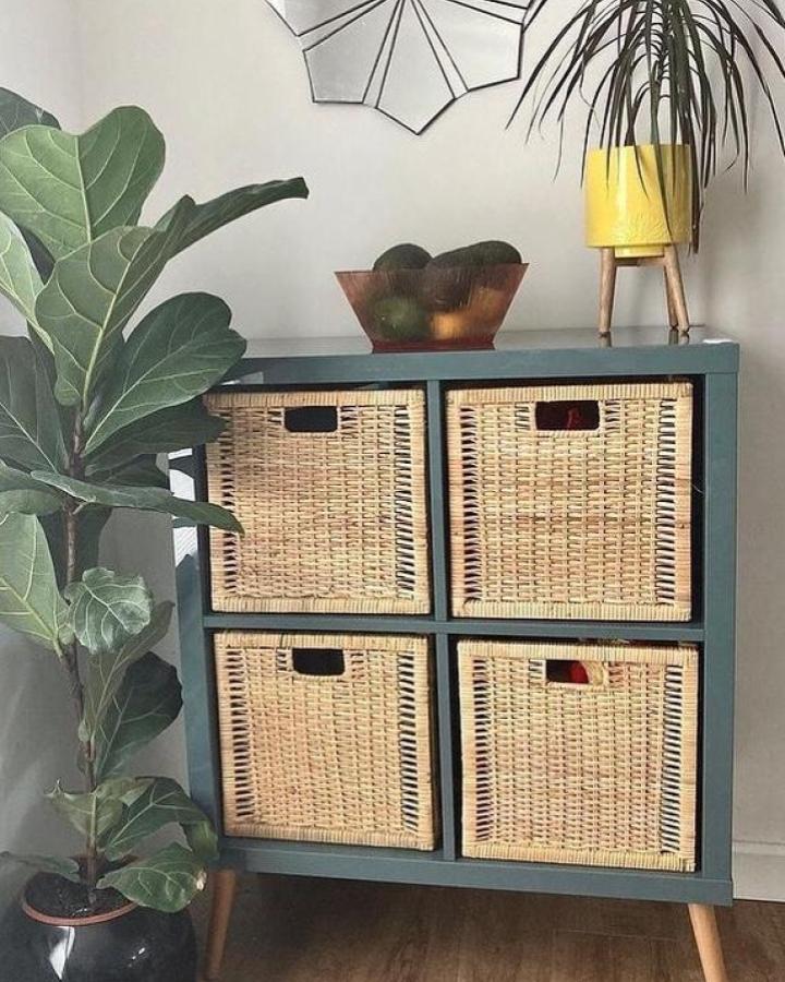 Teal wood shelving unit with woven baskets and wooden legs from @shiftabrick in cozy living space. Stylish storage solution.
