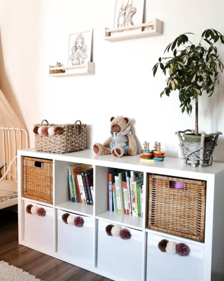 White Ikea Kallax storage with wicker baskets and pom pom drawer handles in neutral tones from @laur.ove ikea kallax hacks for kids room organization.