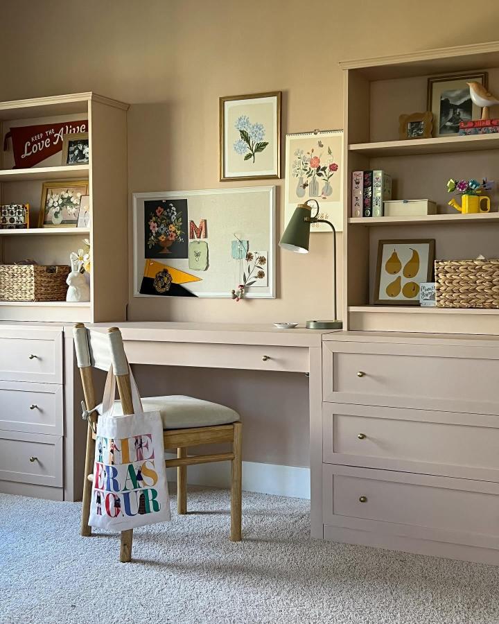 Soft pink built-in desk and storage with brass knobs and warm wood chair from @thegoodmanhouse in cozy workspace design.