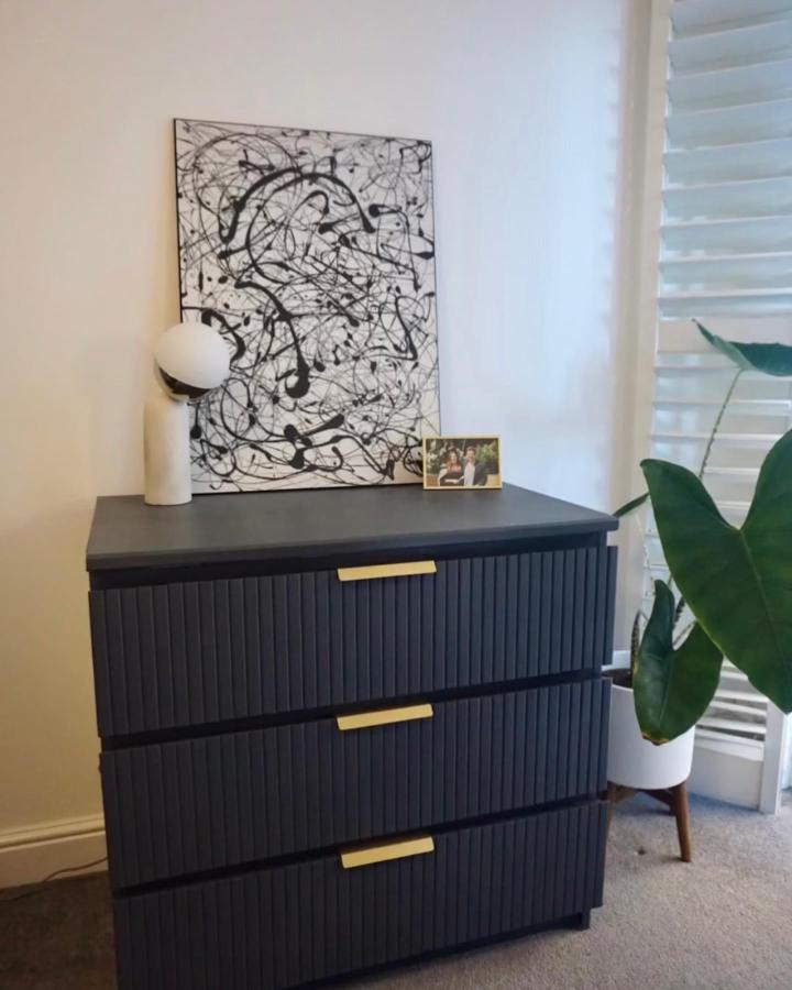 Dark grooved black dresser with brass handles from @elm.abode. Stylish modernized bedroom storage with textured drawer fronts.