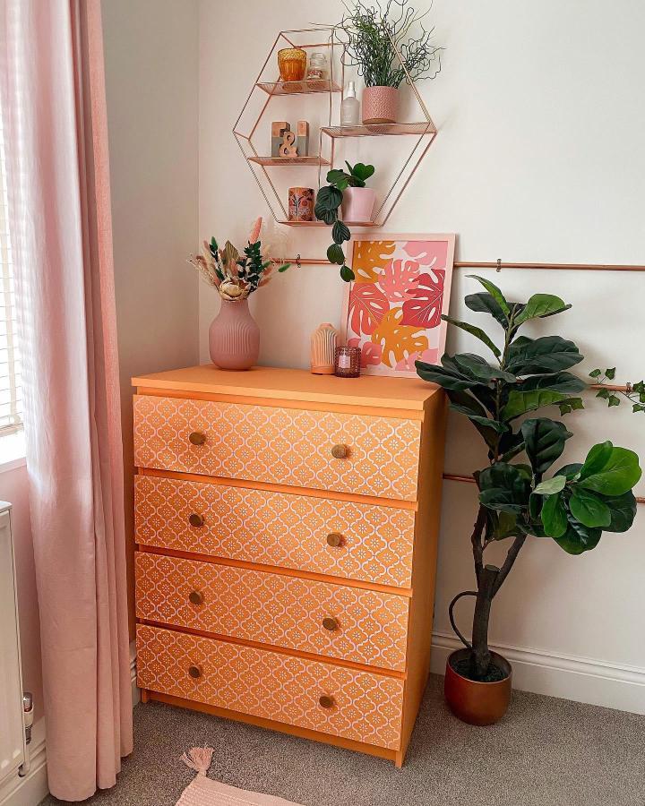 Orange patterned Ikea Malm dresser hack from @sevenpalmtreehouse with brass knobs and cheerful painted finish in a cozy room corner.