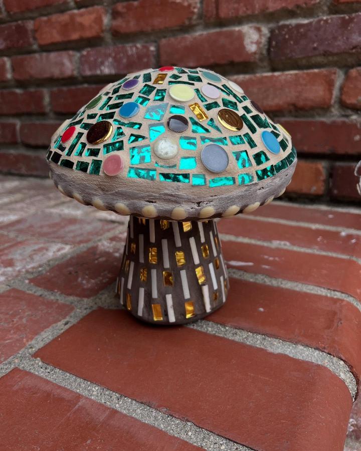 Turquoise and gold glass tile mushroom sculpture on brick surface by @gardentileart with colorful button accents and striped base.