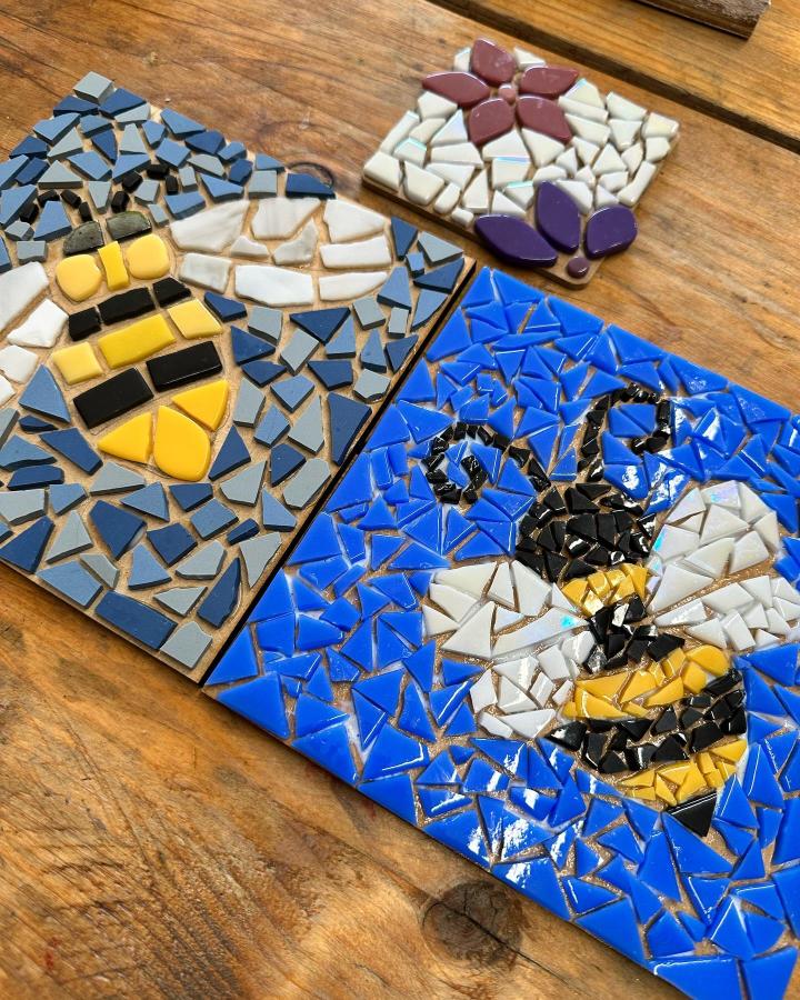 Yellow black and blue bee mosaic tiles on wooden surface from @larkswold featuring playful mosaic tile craft ideas with flower accents.