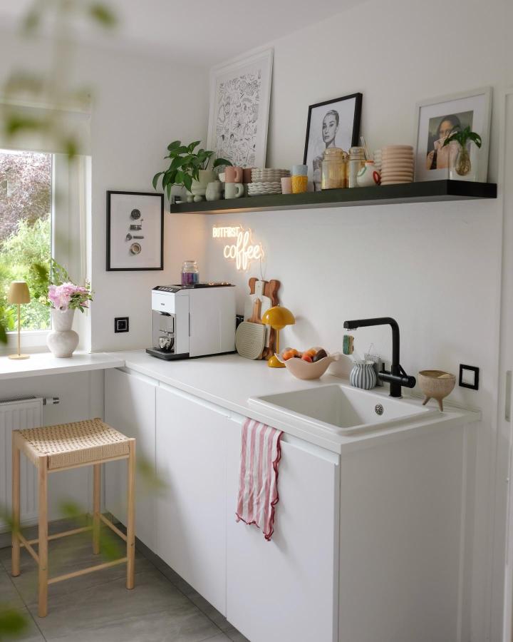 Black floating shelf kitchen open shelving ideas for your kitchen from @ankesummer with ceramics, plants, and neon accent lighting above white cabinets and sink.