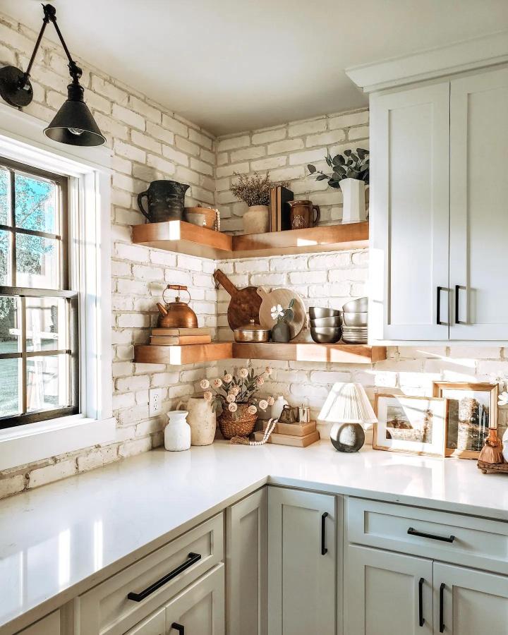Warm wood floating shelves with whitewashed brick wall and natural decor from @theroaringcreekhome. Cozy kitchen corner with rustic charm and simple elegance.