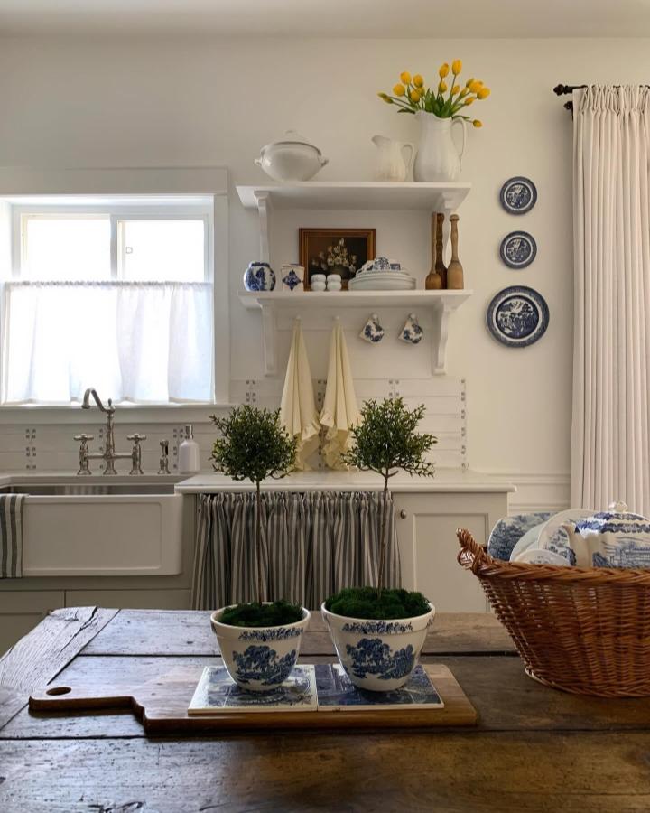 Blue and white farmhouse style kitchen shelves from @billieshumblehome showing vintage china and hanging teacups against cream walls.