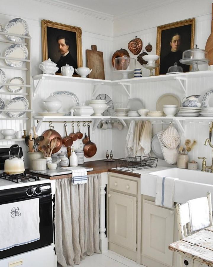 Classic white open shelves and copper cookware in a rustic kitchen by @myriversidefrenchcottage showcasing antique charm and cozy textiles