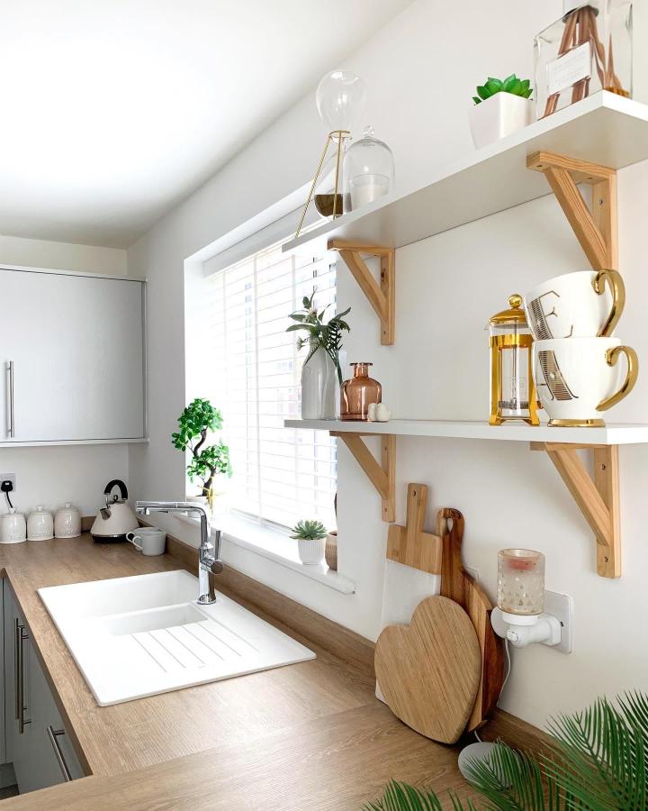 White shelves with natural wood brackets in a bright kitchen space from @our_claytoncorner_. Minimalist style with cozy natural accents.