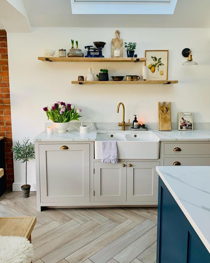 Light oak wood floating shelves in a bright kitchen from @sw20_nest featuring natural elements and brass accents above a white farmhouse sink.