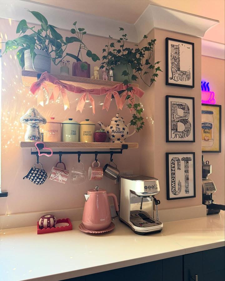 Pink pastel and natural wood open shelving ideas for your kitchen from @tamzinmcgillen featuring tea canisters, mugs, plants, and espresso machine on shelves.
