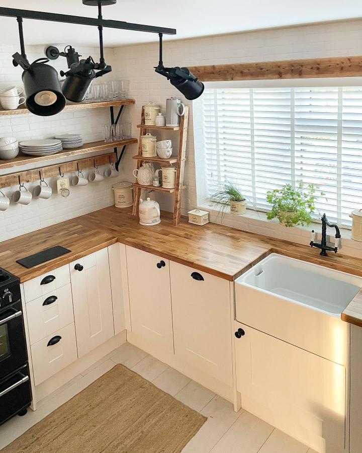 Light rustic wood open shelving ideas for your kitchen from @surreyedit. Warm wood with black metal brackets and cozy mug hooks near farmhouse sink.