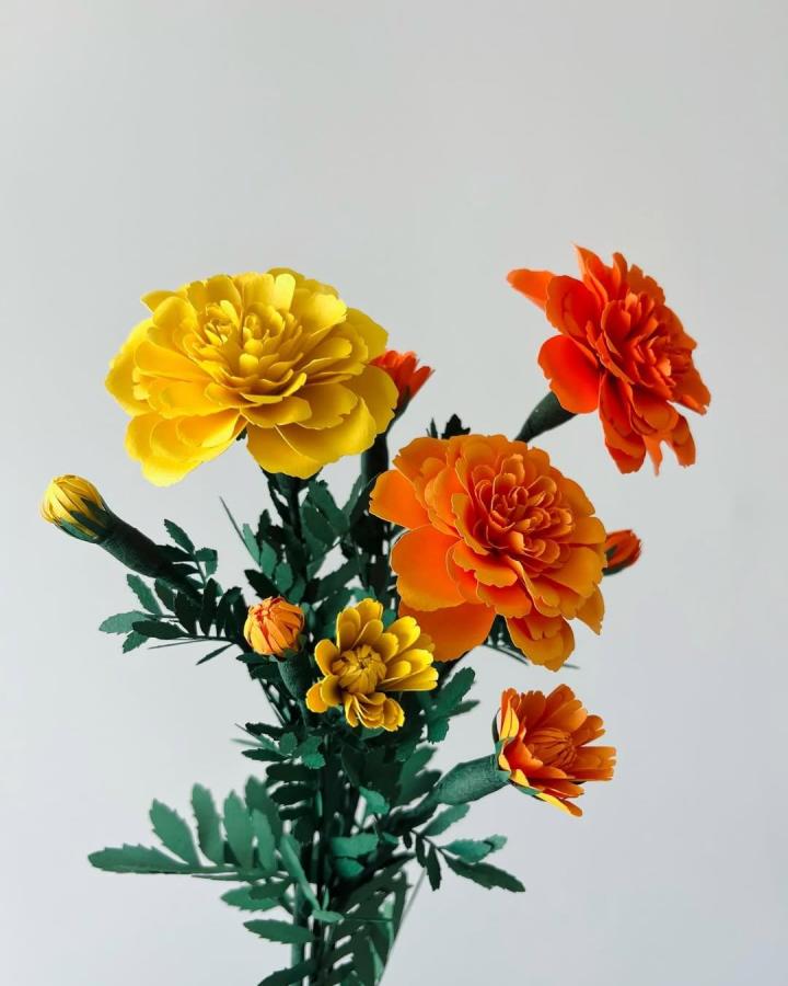 Yellow and orange marigold paper flower crafts for adults from @floret.craft with detailed green leaves and layered petals.