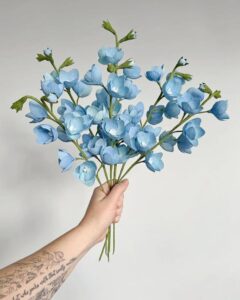 Soft blue crepe paper flower bouquet held by hand from @besspapergoods showing detailed delicate petals and green stems.