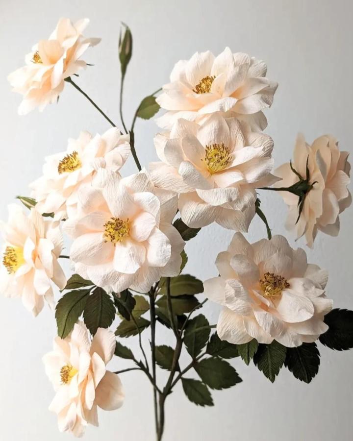 Soft creamy peach crepe paper floral arrangement with green leaves by @papergarden.artstudio delicate handmade blooms with textured petals.