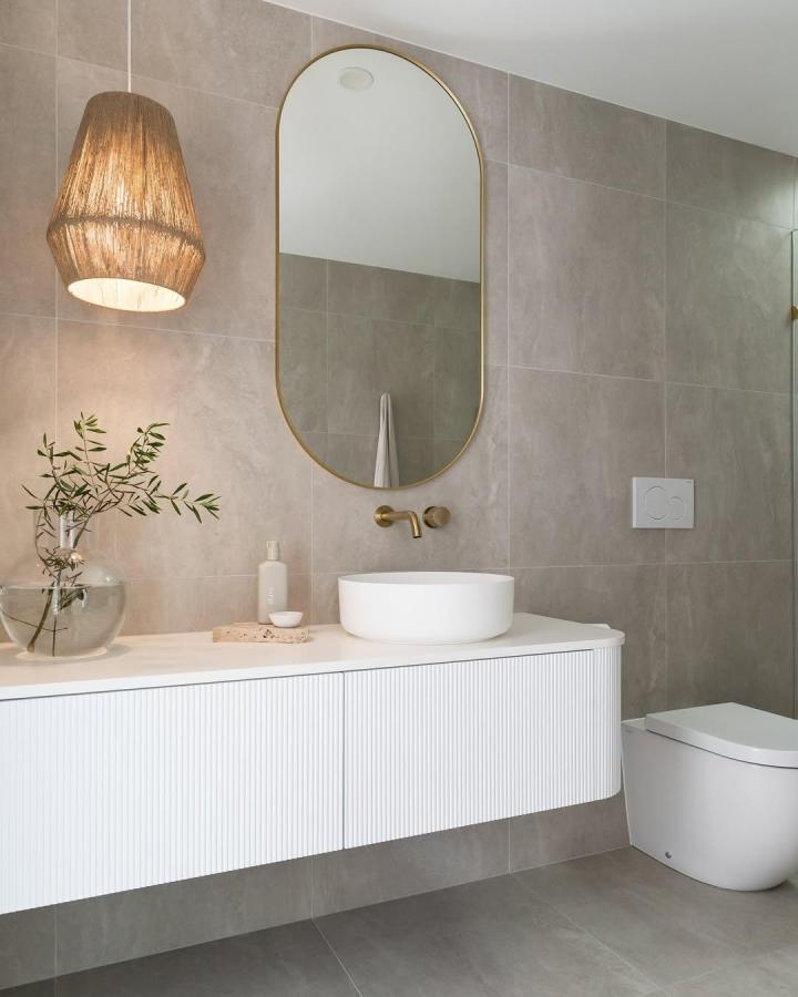 White ribbed floating cabinet in powder room storage ideas by @haausdesign featuring brass fixtures and a round mirror.