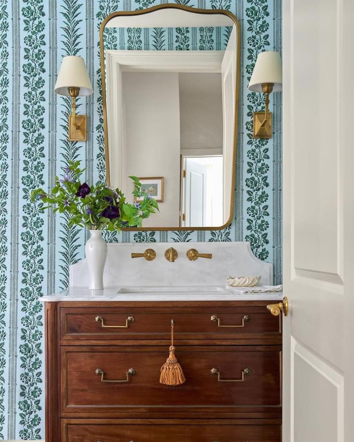 Dark wood vintage vanity with brass hardware and marble top in powder room storage ideas from @jessicalevantiques featuring floral wallpaper and classic mirror.