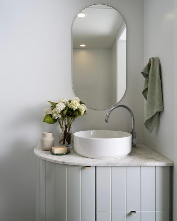 Gray curved wood cabinet with marble top and oval mirror from @christinaprescottdesign. Stylish, minimalist storage solution.