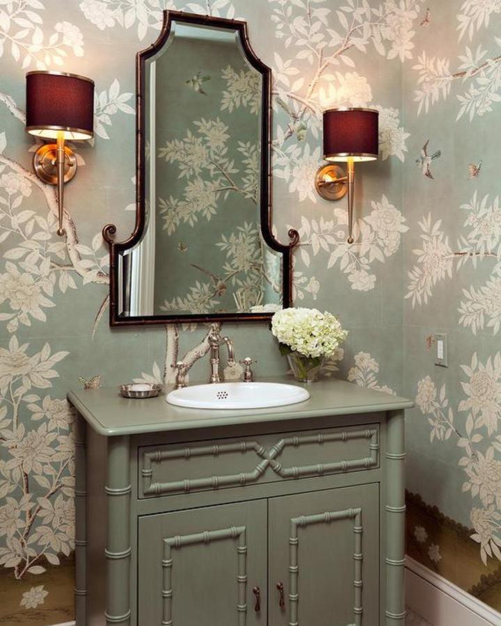 Sage green bamboo-style vanity cabinet in powder room storage ideas by @winstonscollection with floral wallpaper and bronze fixtures.