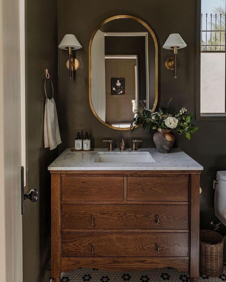 Warm wood vanity with marble top by @mckenziehowarth featuring vintage brass details and clever hidden storage in a cozy bathroom setting.
