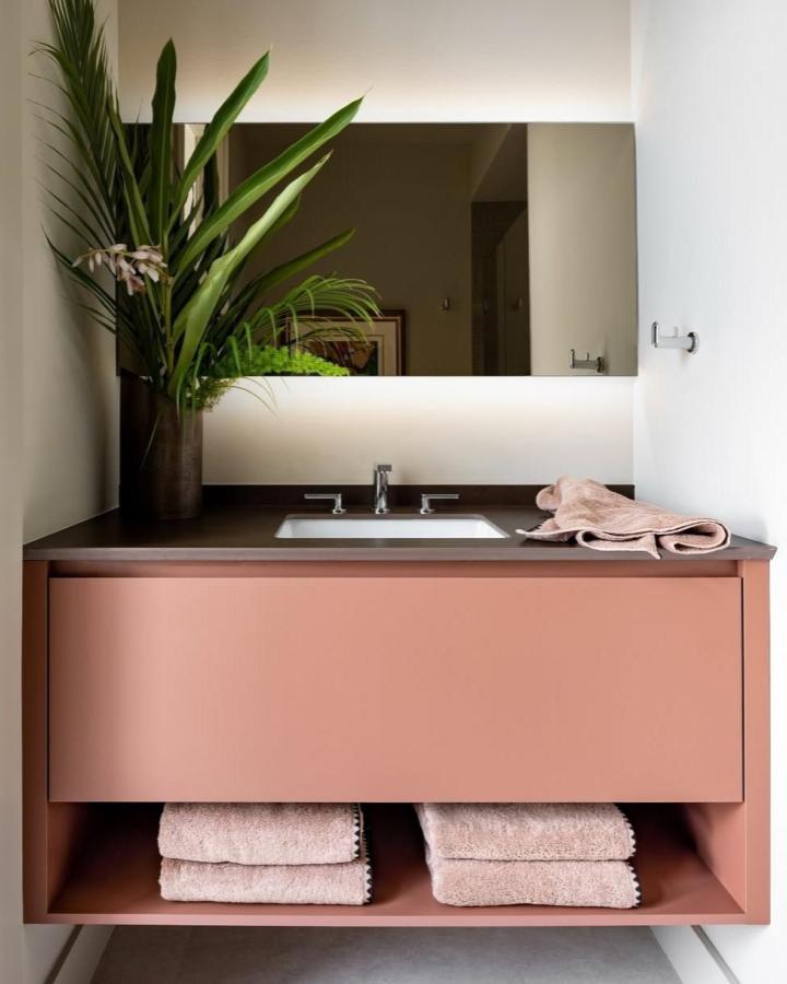 Terracotta floating vanity with open shelf and soft towels from @veemerklen. Modern minimalist powder room storage with greenery.