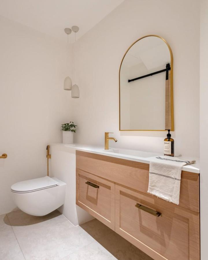 Warm wood floating vanity with gold accents in a minimal powder room by @studio_van_oliver featuring smart powder room storage ideas and a sleek design.