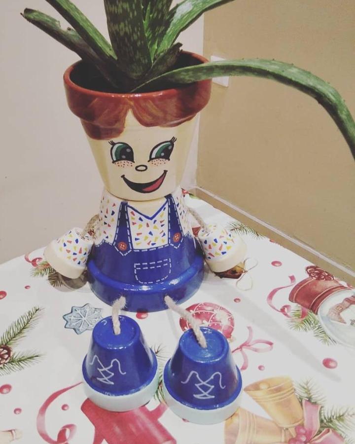 Terracotta pot crafts featuring a colorful whimsical doll planter with painted face and clothing from @craftycreationsmt. Fun and creative plant holder.