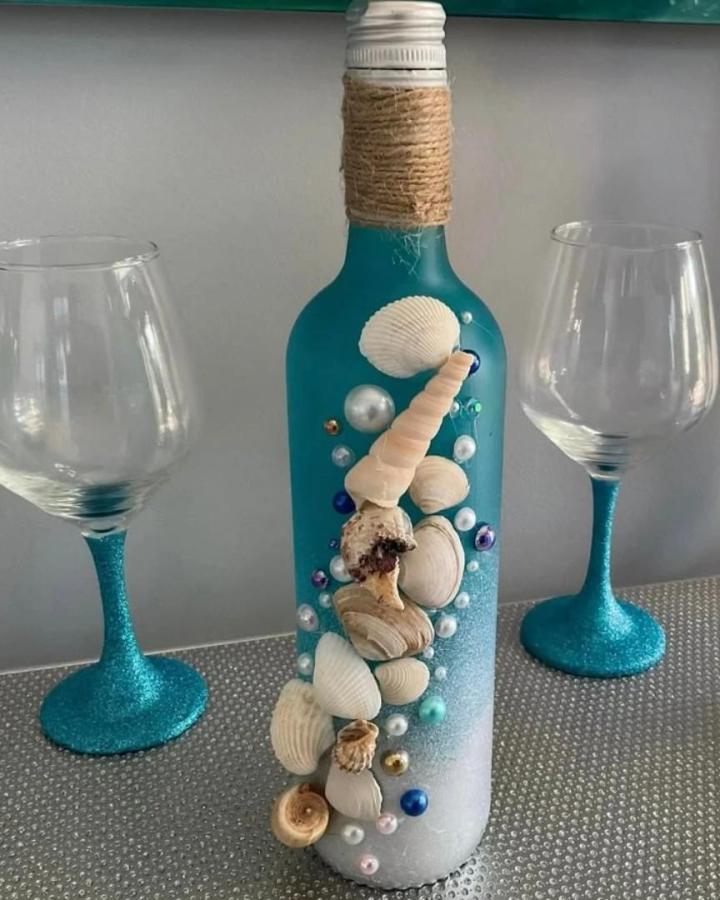Teal seashell bottle craft from @craftykraft1. Beach crafts for adults feature jute, pearls, glitter, and turquoise glassware.
