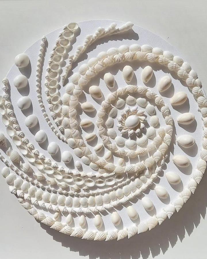 White seashell mandala craft from @mermaids__garden. Layered shells form spirals on a round white base.