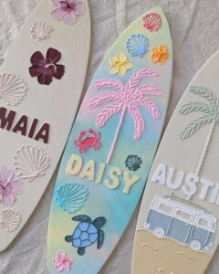 Pastel ombré wooden surfboard plaque from @beyondthepalms_. Raised shells, flowers, palm, turtle, and lettering decorate the design.